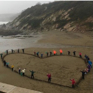 A beach with people stood in a heart shape